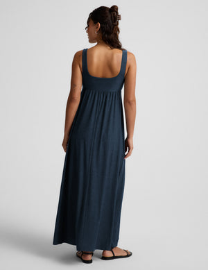 Woman wearing a navy blue sleeveless dress on a light gray background. 
