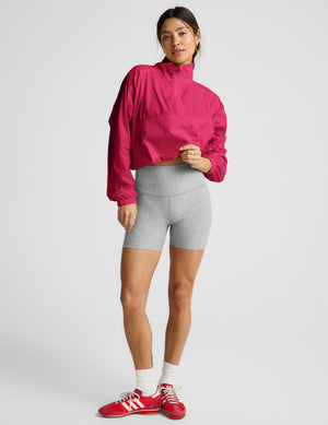 Woman wearing a red half-zip jacket and gray biker shorts against a plain background. 