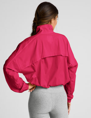 Woman wearing a red half-zip jacket and gray biker shorts against a plain background. 