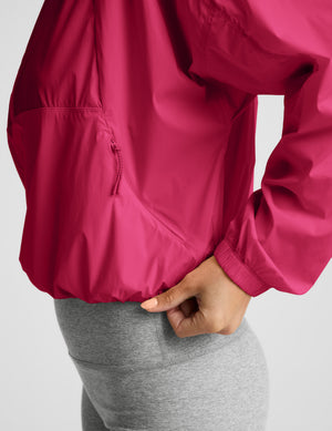 Woman wearing a red half-zip jacket and gray biker shorts against a plain background. 