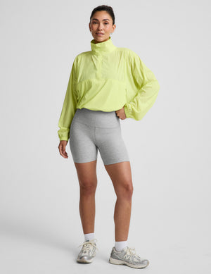 Woman wearing a bright yellow jacket and gray shorts on a light gray background. 