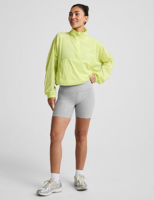 Woman wearing a bright yellow jacket and gray shorts on a light gray background. 