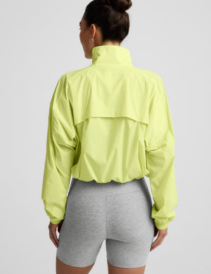 Woman wearing a bright yellow jacket and gray shorts on a light gray background. 