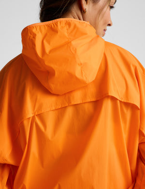 Woman wearing an orange jacket and orange biker shorts against a plain background. 