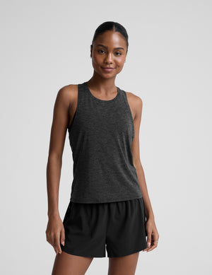 Woman wearing a dark gray tank top and black shorts on a light gray background. 