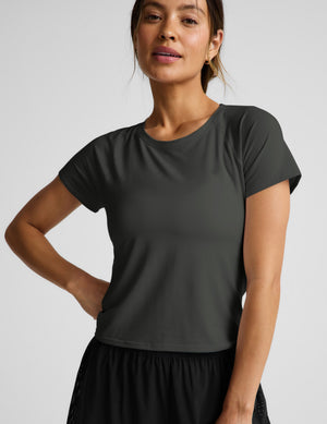 Woman wearing a dark green short sleeve active top and black shorts against a plain background. 