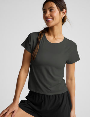 Woman wearing a dark green short sleeve active top and black shorts against a plain background. 