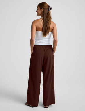 Woman wearing a white halter tank top and brown wide-leg pants on a plain background. 