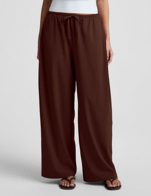 Woman wearing a white halter tank top and brown wide-leg pants on a plain background. 