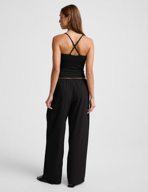 Woman wearing a black tank top and wide-leg pants on a light gray background. 