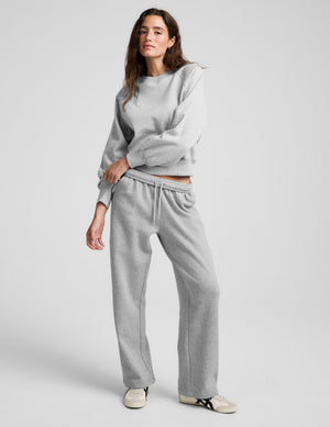 Woman wearing a gray crewneck sweatshirt and gray sweatpants against a plain background. 