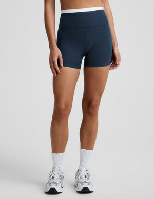 Woman wearing a white sports bra and navy blue biker shorts against a plain background. 