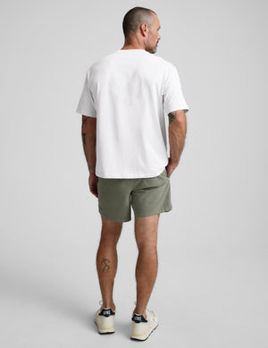 Man wearing a white t-shirt and green shorts on a gray background. 