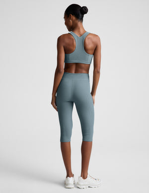 Woman wearing a blue ribbed bra and blue ribbed pedal pushers against a plain background. 