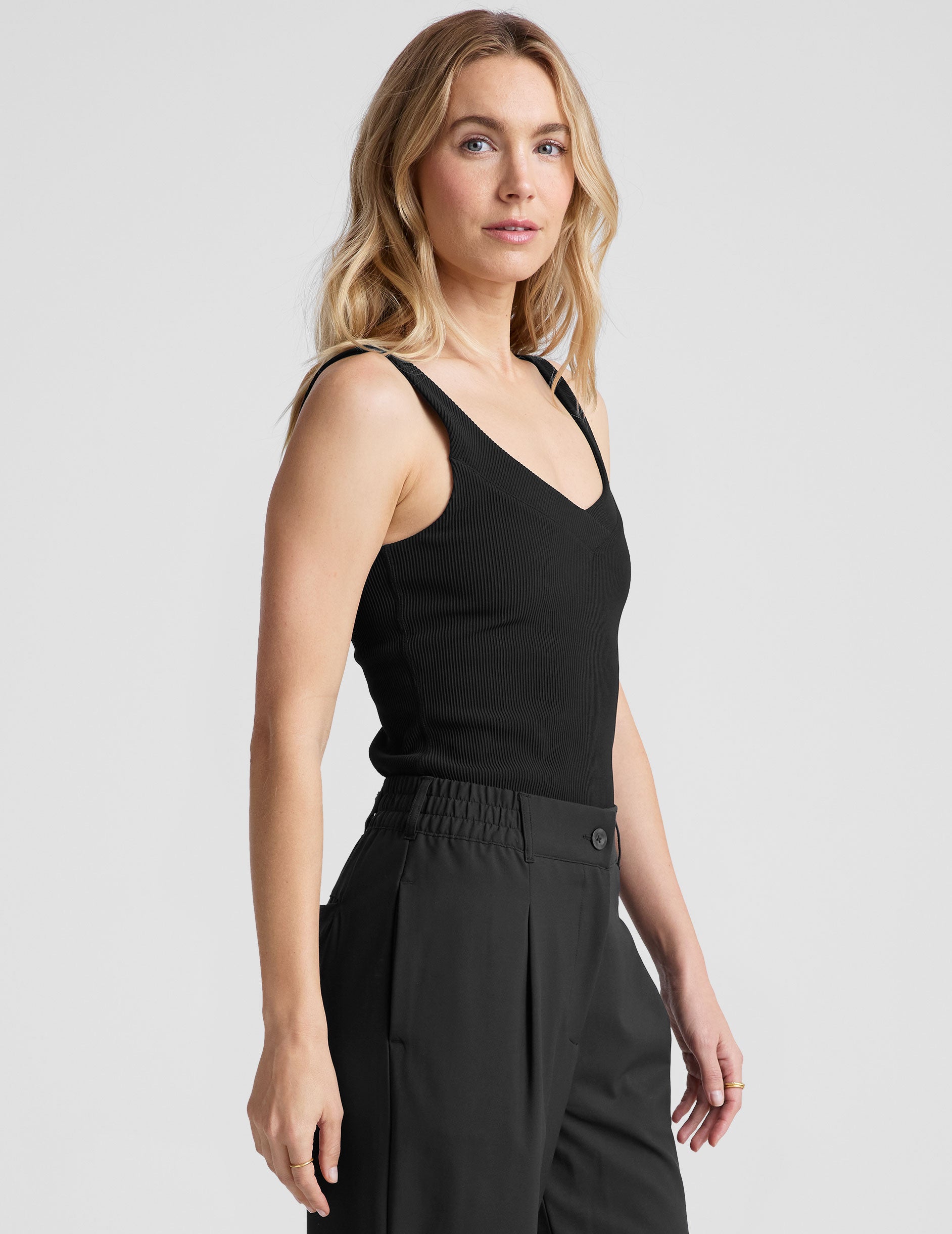 black ribbed tank top with a soft V neckline front and back​, overlapping front neckline detail, and a performance lining shelf bra. Tank hits at a high hip length. 