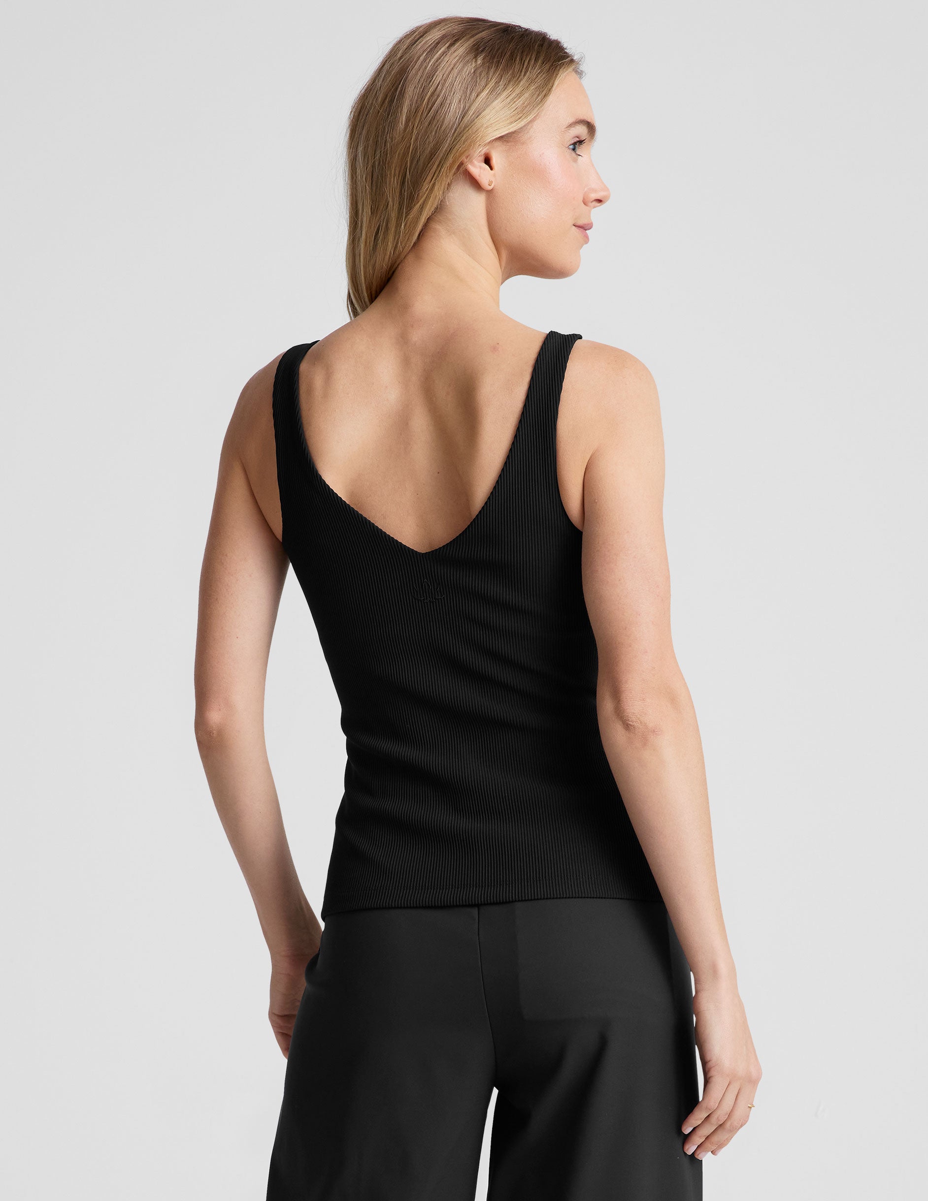 black ribbed tank top with a soft V neckline front and back​, overlapping front neckline detail, and a performance lining shelf bra. Tank hits at a high hip length. 