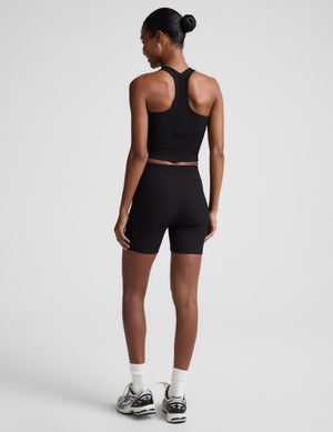 Woman wearing a black tank top and black biker shorts against a plain background. 