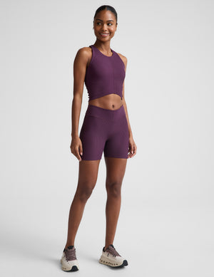 Woman wearing a purple cropped tank and biker shorts against a plain background. 