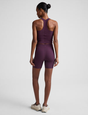 Woman wearing a purple cropped tank and biker shorts against a plain background. 