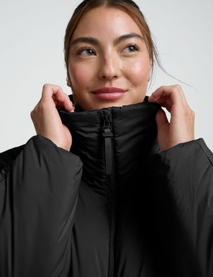 Person wearing a black zip-up puffer jacket and pants on a plain background. 