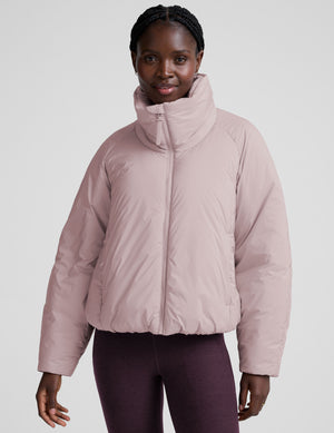 model wearing a light pink puffer jacket on a light background. 