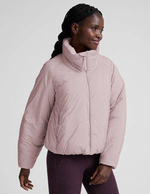 model wearing a light pink puffer jacket on a light background. 