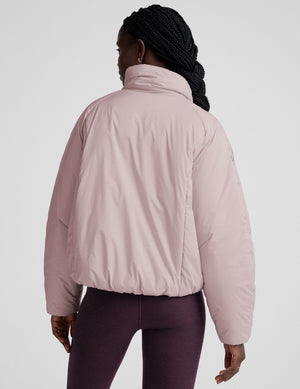 model wearing a light pink puffer jacket on a light background. 