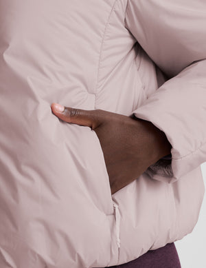model wearing a light pink puffer jacket on a light background. 