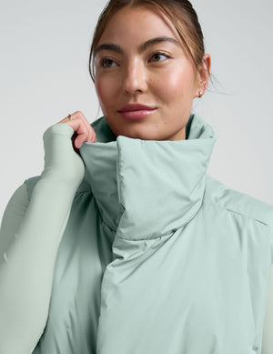 Woman wearing a light blue cropped puffer vest on a plain background. 