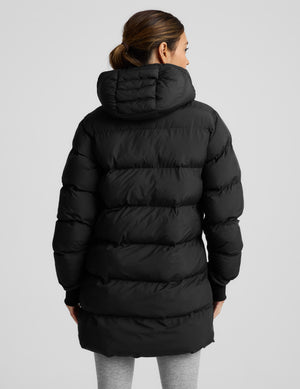 Person wearing a black puffer coat on a light gray background. 