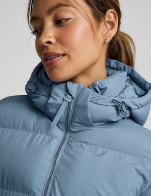 Woman wearing a blue mid length puffer coat on a light gray background. 