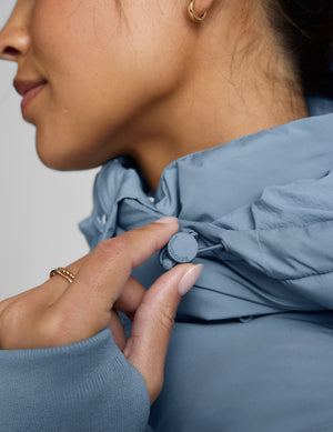 Woman wearing a blue mid length puffer coat on a light gray background. 