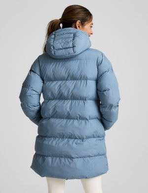 Woman wearing a blue mid length puffer coat on a light gray background. 