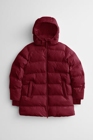 woman wearing a red mid thigh length puffer jacket with a hood against a snowy background. 