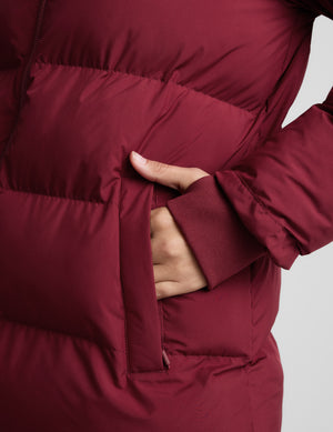 Woman wearing a red mid length puffer coat on a light gray background. 