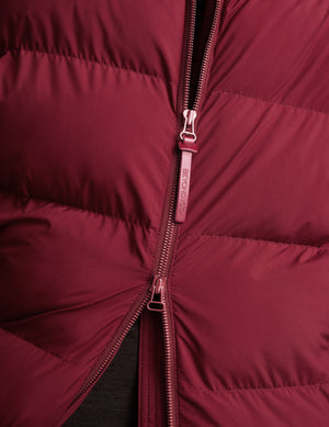 Woman wearing a red mid length puffer coat on a light gray background. 