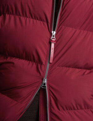 Woman wearing a red puffer coat on a light gray background. 