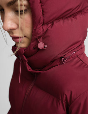 Woman wearing a red mid length puffer coat on a light gray background. 