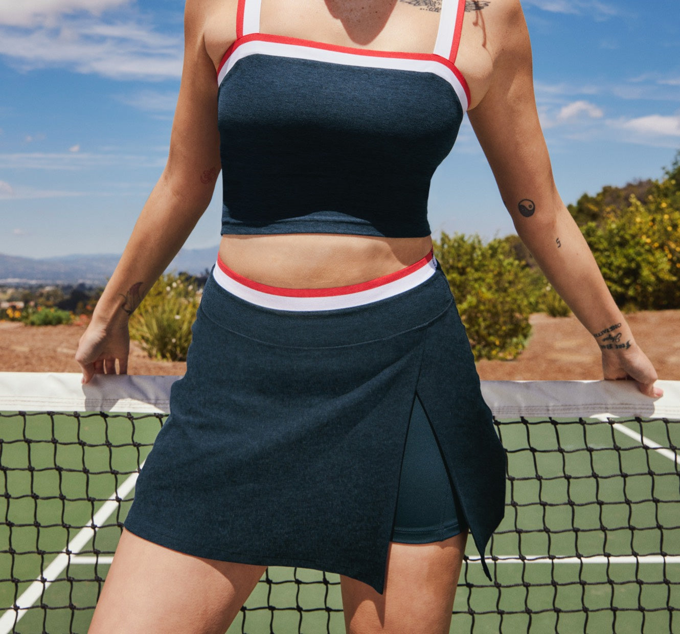 model is wearing a blue cropped tank top with white and red outline details and a blue mini skirt with a front side slit that has red and white outline details. 