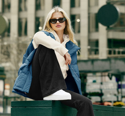 model is wearing a white hoodie, blue zip-up puffer jacket, and black high-waisted flare leggings. 