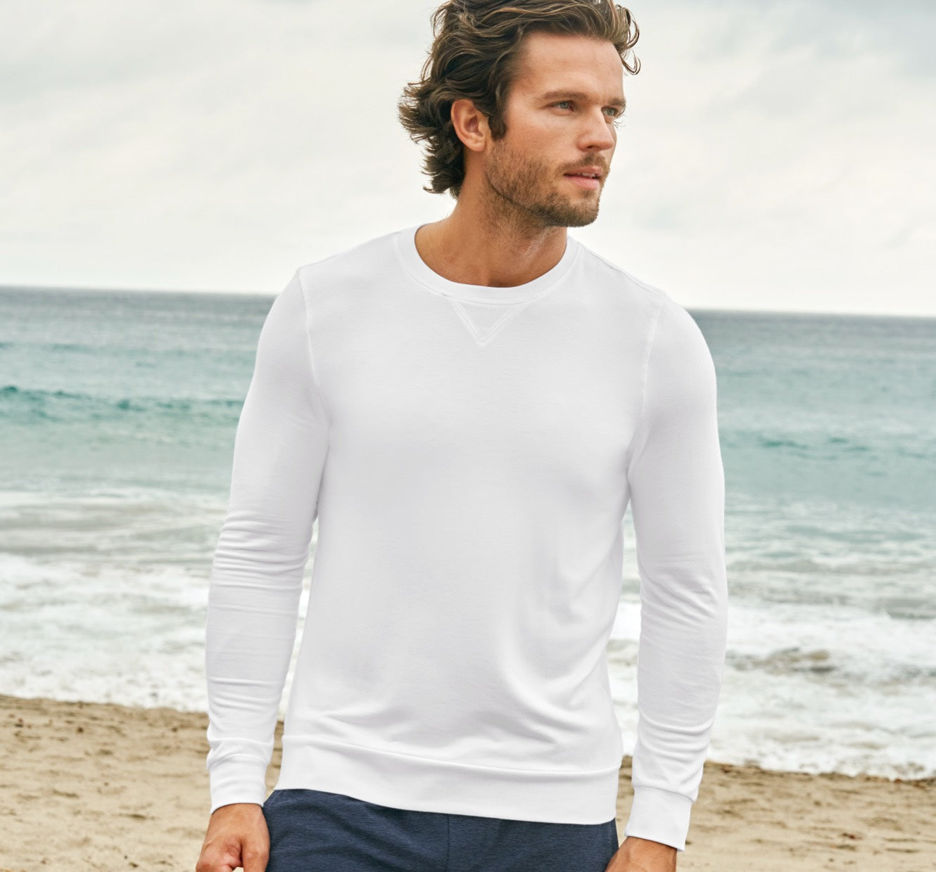 model is wearing a white men's long sleeve top and blue men's shorts. 