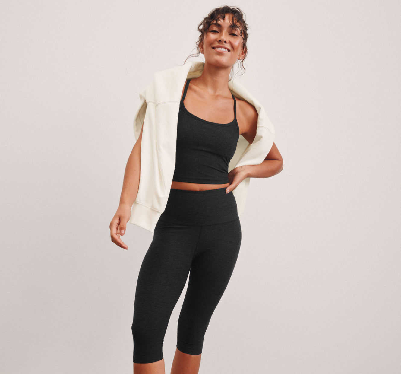 model is wearing a black racerback cropped tank and pedal pusher length leggings. 