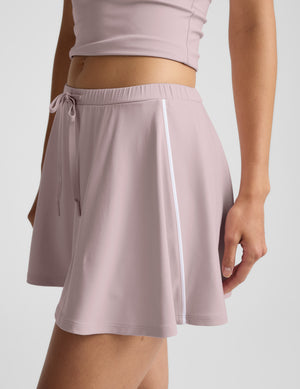 Woman in a pink polo tank and skirt against a plain background. 