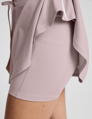 Woman in a pink polo tank and skirt against a plain background. 