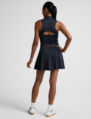 Woman in a navy cropped tank and navy skirt against a plain background. 