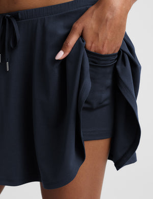 Woman in a navy cropped tank and navy skirt against a plain background. 