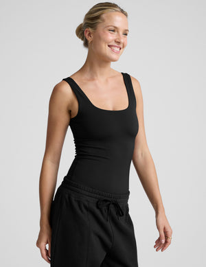 woman wearing a black tank bodysuit and black pants against a plain background. 