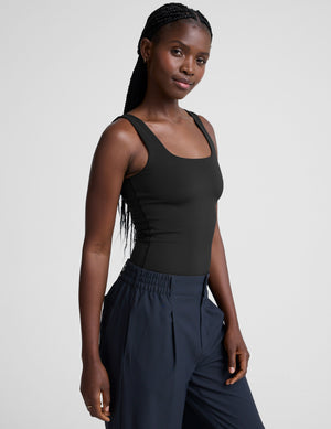 model is wearing a black double-layered square neckline bodysuit and blue trousers against a light gray background. 