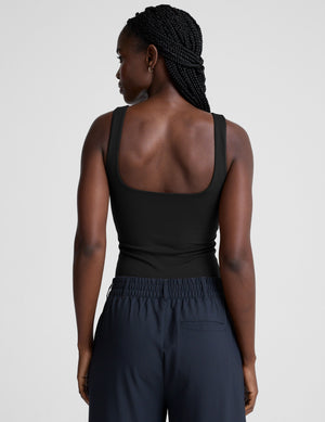 model is wearing a black double-layered square neckline bodysuit and blue trousers against a light gray background. 