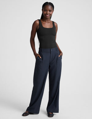 model is wearing a black double-layered square neckline bodysuit and blue trousers against a light gray background. 